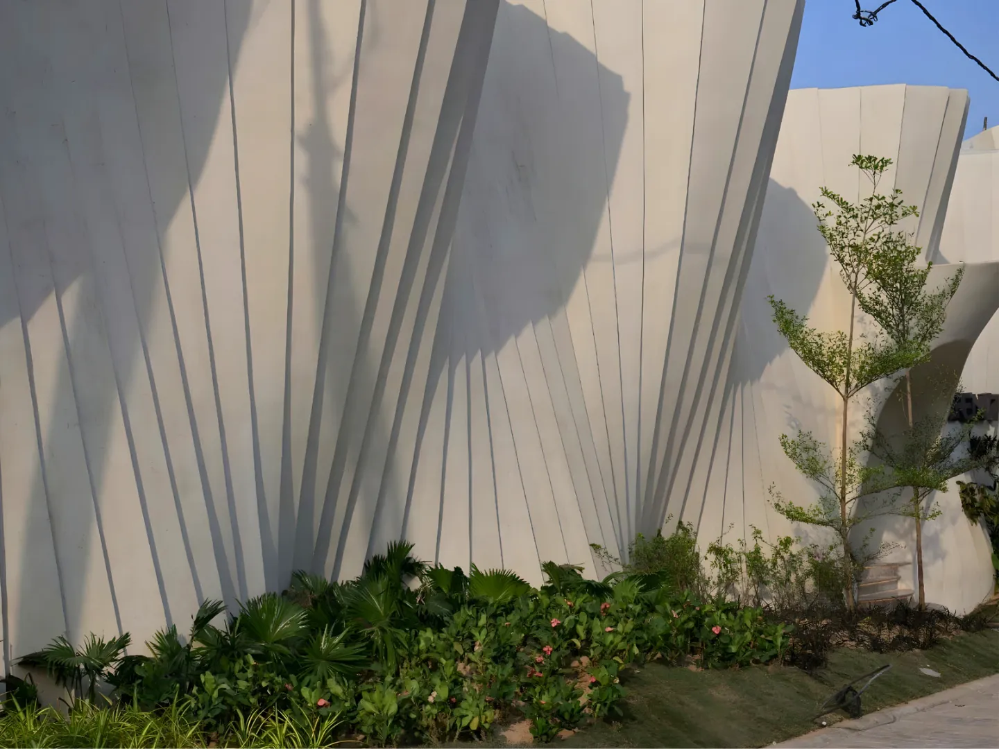 Angled facade fins casting patterned shadows above planted edges.