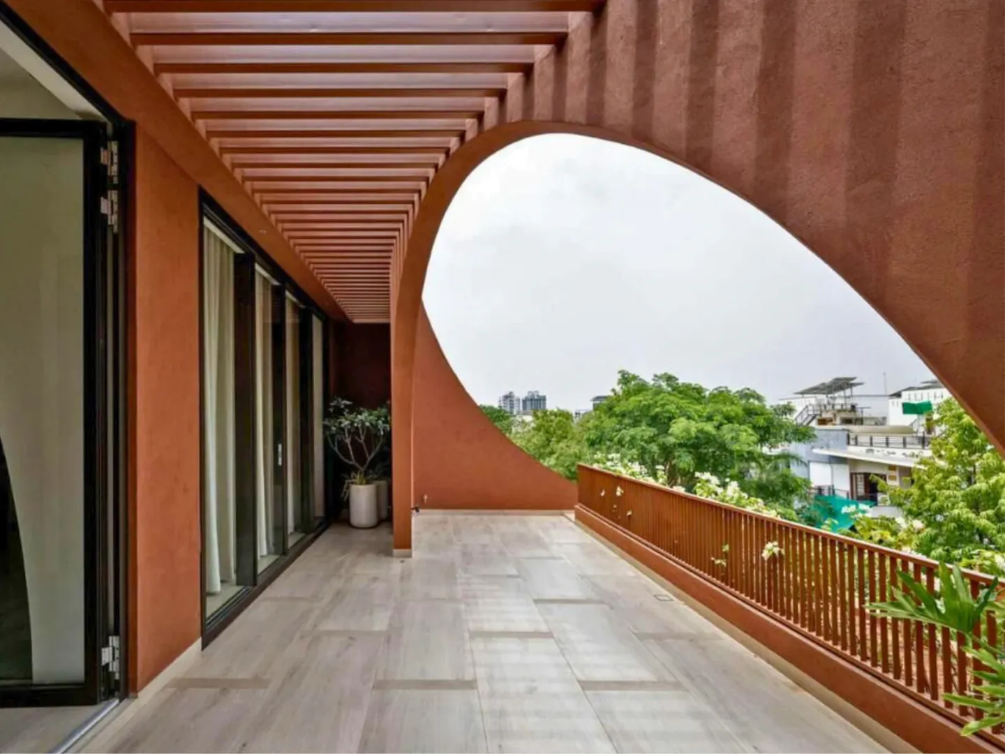 Curved red exterior wall forming a sheltered threshold beside glazed interior spaces.