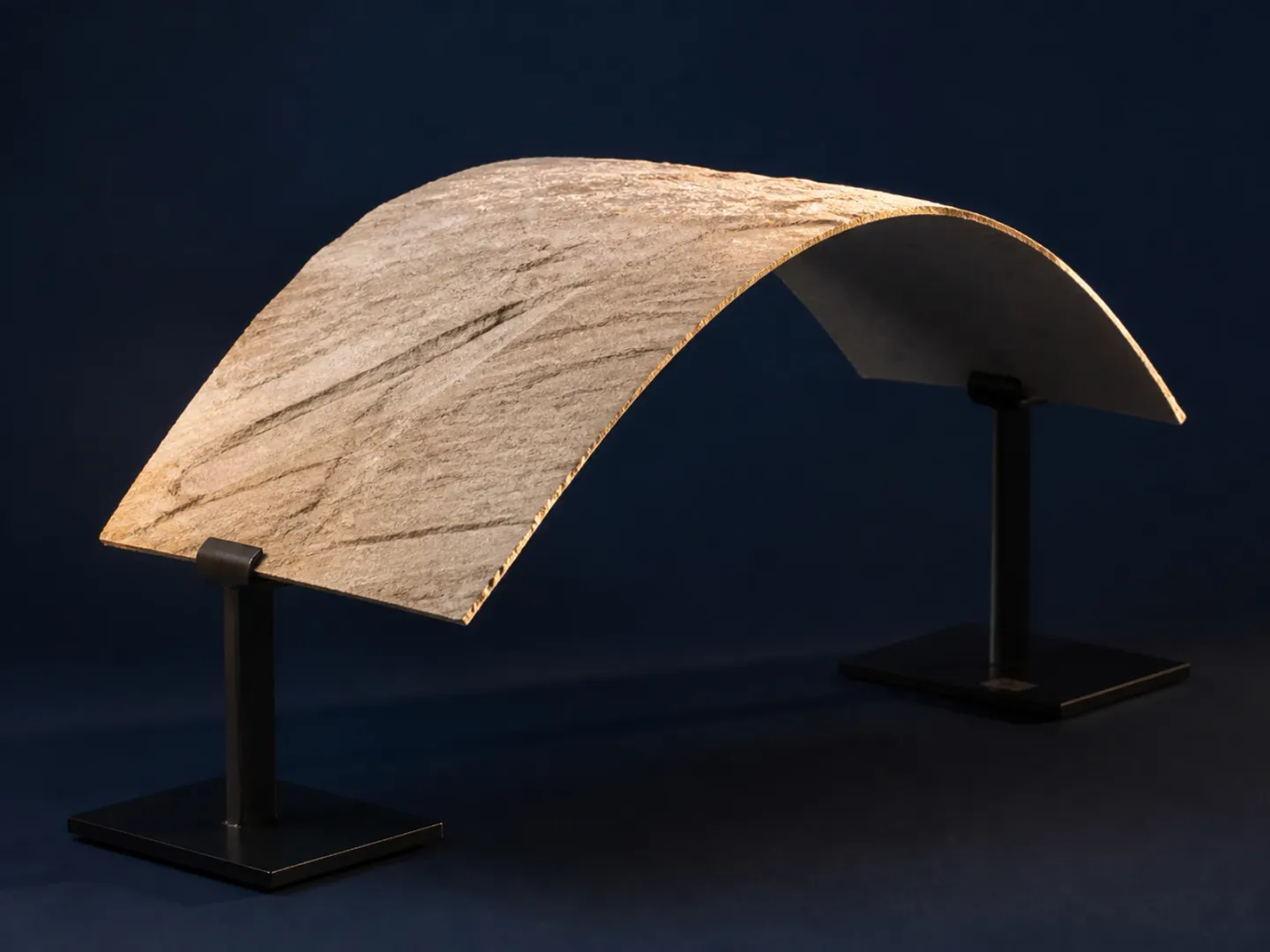 A thin real-stone veneer sheet flexed into an arc on dark stands.