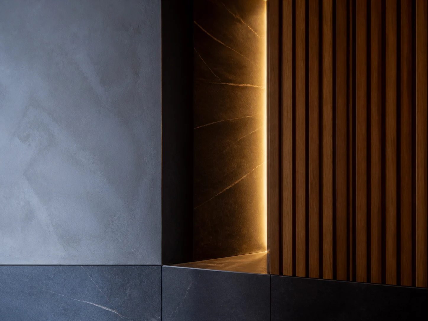 Mineral plaster, dark stone and vertical timber slats meeting at an illuminated interior corner.