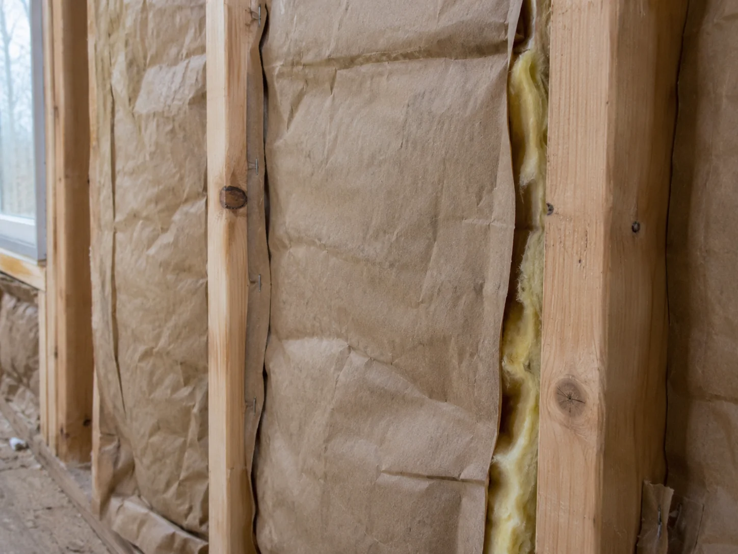 Brown kraft facing on fibrous insulation between timber studs, with a folded flange against the wood.