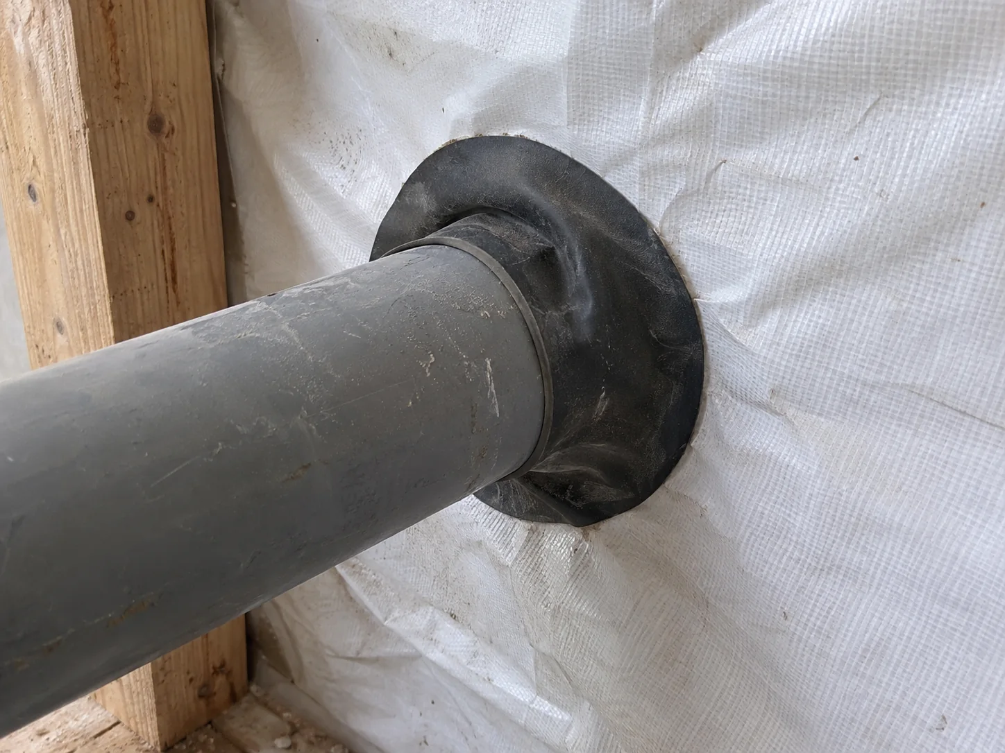 Gray service pipe passing through a white membrane with a dark collar around the pipe.